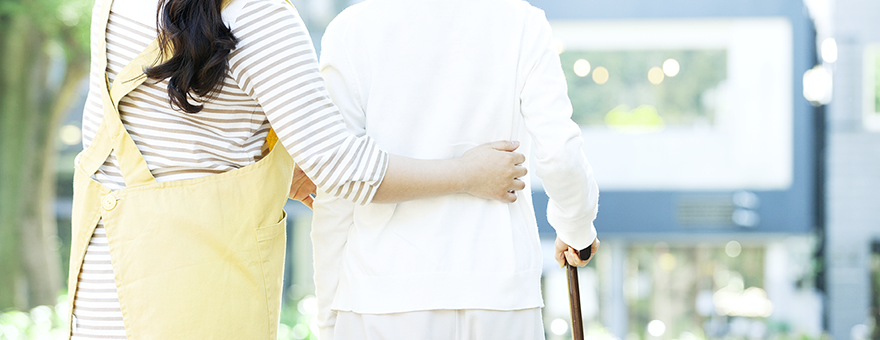 Photo of a female staff supporting an elderly woman with her hand on her waist